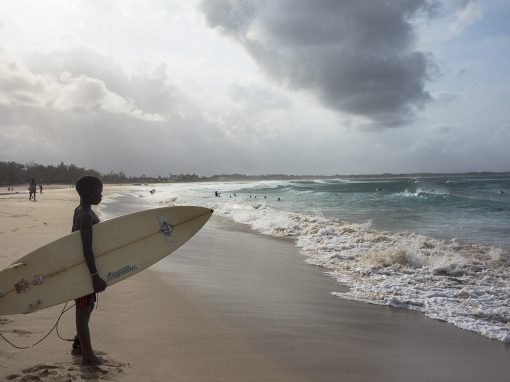 Pojken står vid strandkanten med surfbräda under armen